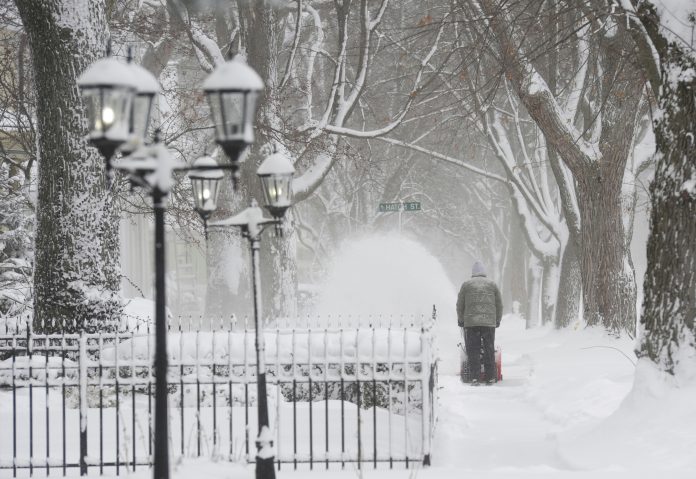 A man clears snow along a sidewalk on State Street in St. Joseph, Mich., Monday, Jan. 15, 2024. Residents are digging out after a winter storm moved across the state with blowing and drifting snow and temperatures in the single digits. (Don Campbell/The Herald-Palladium via AP)