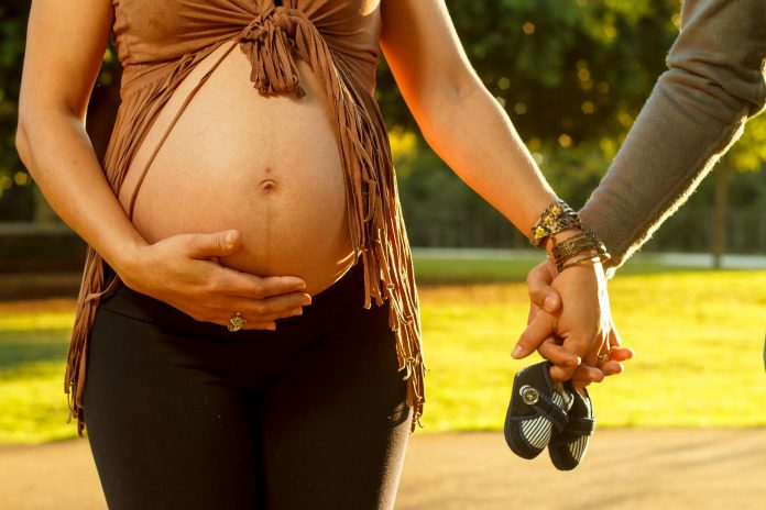 pregnant woman holding man hand and baby shoes