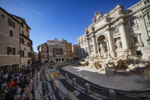 Visitors throw coins into a temporary pool while the Trevi Fountain in Rome is being repaired