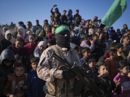 A Hamas fighter stands next to a crowd as before the hand-over of Israeli and Thai hostages to the Red Cross in the south Gaza Strip town of Khan Younis, Thursday Jan. 30, 2025.(AP Photo/Abdel Kareem Hana)