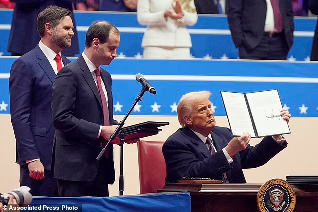 President Donald Trump signs executive orders on stage at an indoor Presidential Inauguration parade event in Washington

