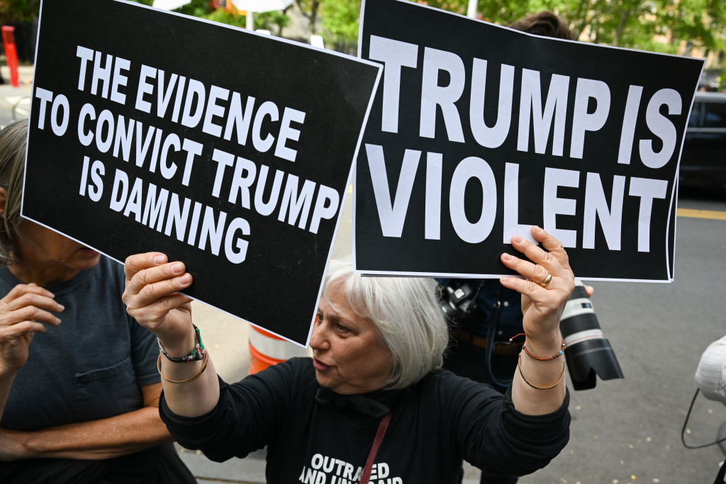 NEW YORK, NEW YORK - MAY 09: : A protester holds up signs outside a Manhattan Federal Court after a jury found former President Donald Trump liable for sexually abusing E. Jean Carroll in a Manhattan department store in the 1990's on May 09, 2023 in New York City. The jury awarded her $5 million in damages for her battery and defamation claims. Carroll has testified that she was raped by Trump, giving details about the alleged attack in the mid-1990s. Trump had stated that the attack never happened and has denied meeting her. He did not taken the stand during the trial. (Photo by Alexi Rosenfeld/Getty Images)