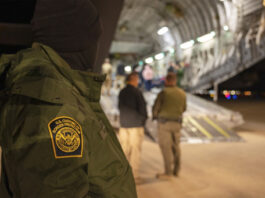 This photo provided by the U.S. Dept. of Defense, A U.S. Customs and Border Protection agent watches as undocumented immigrants are loaded onto a C-17 Globemaster III at Tucson International Airport in Tucson, Ariz., Thursday, Jan. 23, 2025. (Senior Airman Devlin Bishop/Dept. of Defense via AP)