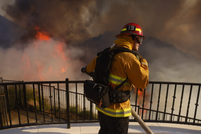 A firefighter makes a stand in front of the advancing Palisades Fire in the Pacific Palisades neighborhood of Los Angeles, Tuesday, Jan. 7, 2025. (AP Photo/Etienne Laurent)