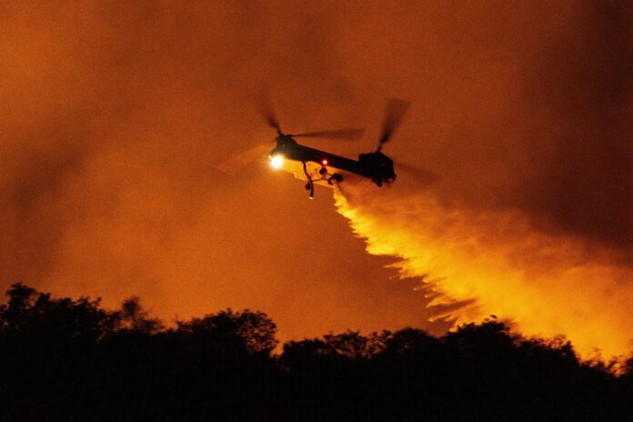 A helicopter drops water on the Palisades Fire in Mandeville Canyon, Saturday, Jan. 11, 2025, in Los Angeles.(AP Photo/Etienne Laurent)