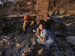 Ella Venne, front, holds a cup she found in the remains of her family's home destroyed by the Eaton Fire as she searches with Glendale Fire Department captain Chris Jernegan, left, and his wife Alison in Altadena, Calif., Saturday, Jan. 11, 2025. (AP Photo/Mark J. Terrill)