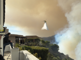 A helicopter unloads water over a fire threatening houses in the Maneville Canyon