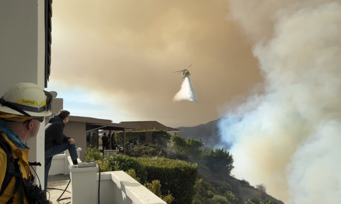 A helicopter unloads water over a fire threatening houses in the Maneville Canyon