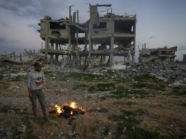 A man stands by a fire next to a destroyed house in an area littered with rubble from buildings demolished during the Israeli army's ground and air offensive against Hamas in Gaza City, Tuesday Feb. 4, 2025.(AP Photo/Abdel Kareem Hana)