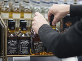 A B.C. Liquor Store employee demonstrates removing bottles of American whiskey for media before a news conference in Vancouver, B.C., Sunday, Feb. 2, 2025. (Ethan Cairns/The Canadian Press via AP)