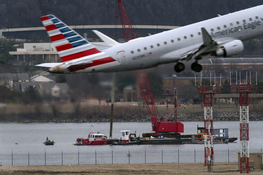 An American Eagle jet passes as rescue and salvage crews work near the wreckage of an American Airlines jet in the Potomac River from Ronald Reagan Washington National Airport, Sunday, Feb. 2, 2025, in Arlington, Va. (AP Photo/Jose Luis Magana)