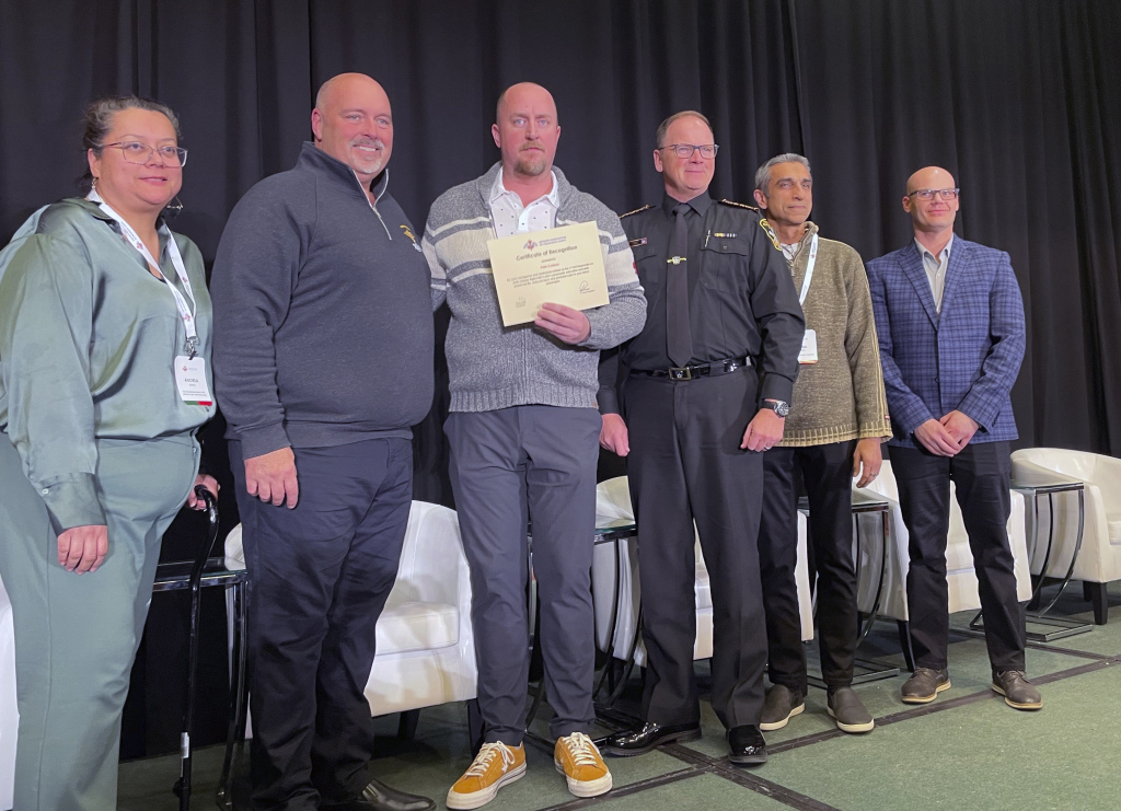 Pete Carlson, third from left, a passenger on the Delta flight that crashed in Toronto on Monday, holds a certificate of recognition for his actions in helping evacuate the plane and help fellow passengers, Wednesday, Feb. 19, 2025 in Toronto, Canada. (AP Photo/John Wawrow)