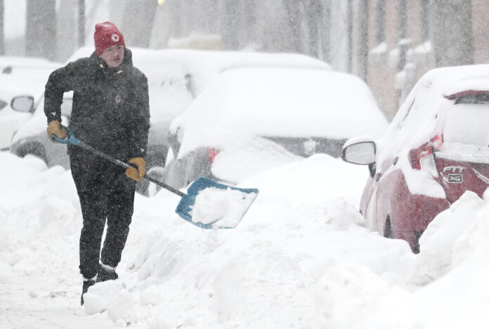 A person clears snow from around a car during a snowstorm in Montreal, Sunday, Feb. 16, 2025. (Graham Hughes/The Canadian Press via AP)