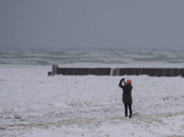 A person takes pictures as they walk on a beach along the shore of Lake Michigan, Wednesday, Feb. 12, 2025, in Chicago. (AP Photo/Kiichiro Sato)