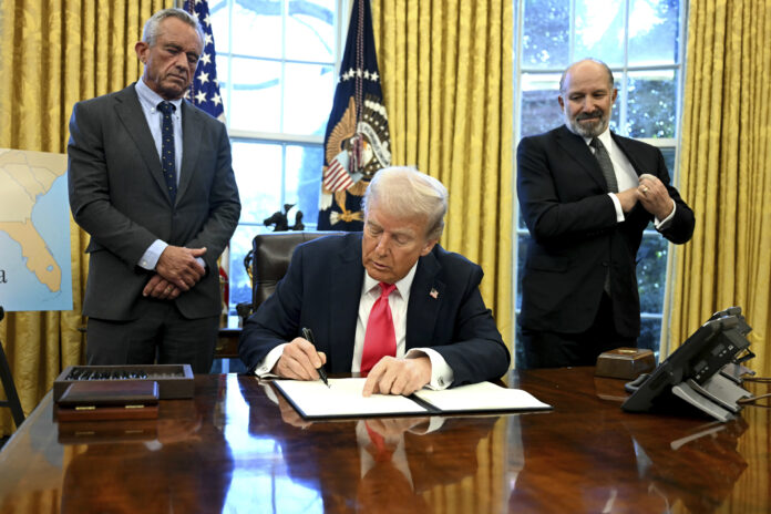 President Donald Trump signs an executive order as Health and Human Services Secretary Robert F. Kennedy Jr., left, and Commerce Secretary Howard Lutnick watch in the Oval Office at the White House in Washington, Tuesday, Feb. 25, 2025. (Pool via AP)